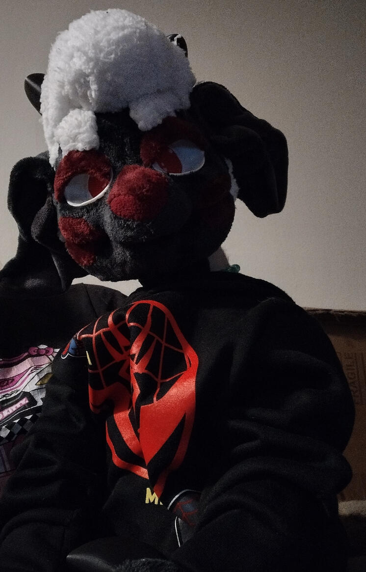 Blackfured white wooled and red cheeks patched Sheep puppet wearing blue jeans and a spiderman hoodie